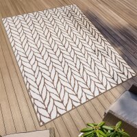 Rechteckiger Outdoor-Teppich mit hellem, beigem Hintergrund und braunem Blättermuster, ausgelegt auf einer Holzterrasse. In der Ecke des Bildes sind Teile von Gartenmöbeln und eine grüne Pflanze zu sehen.