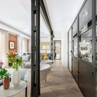 Eine Frau spielt lachend mit zwei kleinen Mädchen barfuß auf einem hellen Holzboden in einem Wohnzimmer, während im Hintergrund ein Mann zuschaut; darüber steht der Schriftzug „Trittschalldämmung und angenehmer Laufkomfort“.