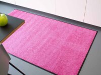Rechteckige Fußmatte mit lilafarbener, flauschiger Oberfläche und schwarzem, rutschfestem Rand auf weißem Hintergrund.