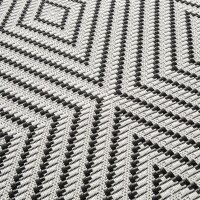 Nahaufnahme eines gewebten Teppichs mit geometrischem Muster aus schwarzen und weißen Linien, die in eckigen, konzentrischen Mustern angeordnet sind.