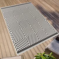 Schwarz-weißer Teppich mit geometrischem Muster aus verschachtelten Rauten auf einer Holzterrasse, im Vordergrund Teile von Gartenmöbeln und einer grünen Pflanze.