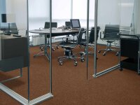 Modernes Besprechungszimmer mit Glaswänden, braunem Teppichboden, einem ovalen Konferenztisch, mehreren schwarzen Bürostühlen auf Rollen, einem Laptop, Arbeitsmaterialien auf dem Tisch und Tageslicht von großen Fenstern.